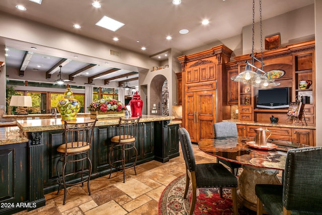 kitchen with light stone countertops, a large island, hanging light fixtures, beamed ceiling, and a breakfast bar