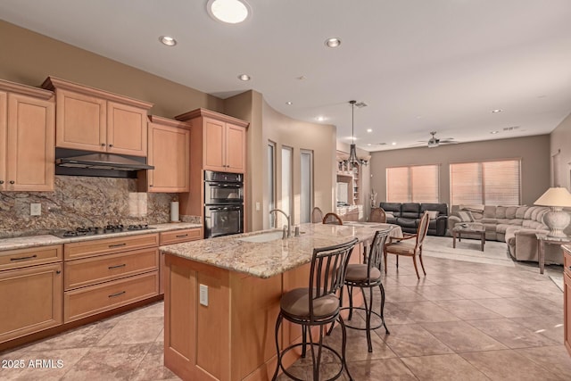 kitchen featuring gas stovetop, multiple ovens, backsplash, a breakfast bar, and an island with sink