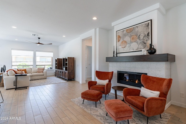 living room featuring a tiled fireplace, ceiling fan, and light hardwood / wood-style flooring