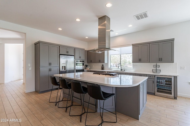 kitchen with a spacious island, sink, island range hood, appliances with stainless steel finishes, and beverage cooler