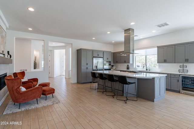 kitchen with island exhaust hood, gray cabinets, beverage cooler, and a center island