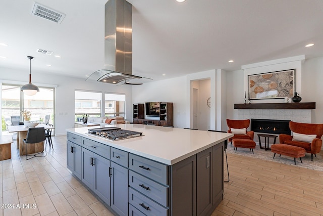 kitchen with pendant lighting, a kitchen breakfast bar, a center island, island range hood, and stainless steel gas cooktop