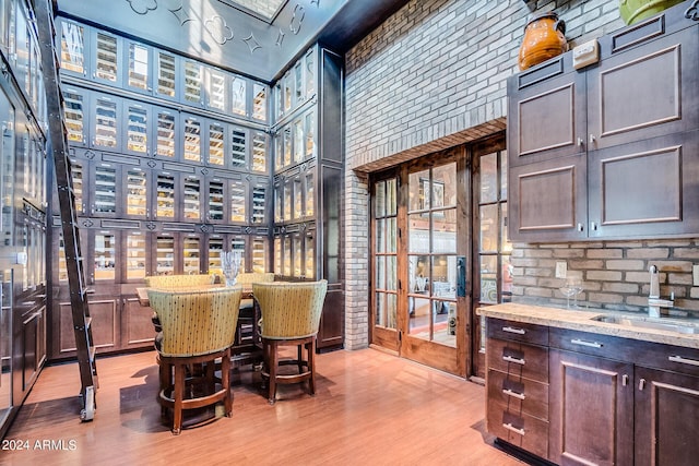 bar with a towering ceiling, sink, light stone counters, dark brown cabinets, and light wood-type flooring