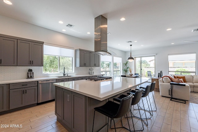 kitchen featuring island range hood, sink, decorative backsplash, hanging light fixtures, and stainless steel appliances