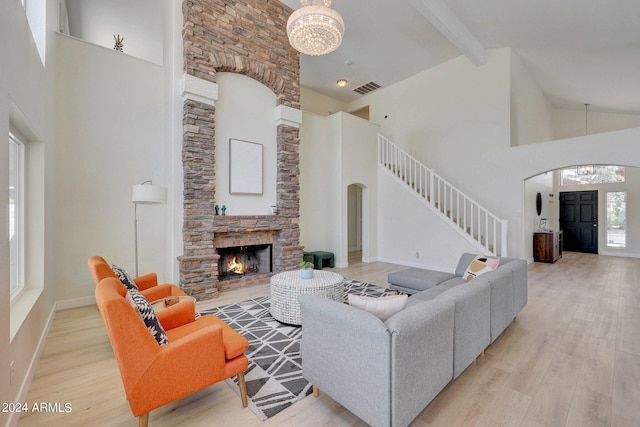 living room with an inviting chandelier, light wood-type flooring, a stone fireplace, high vaulted ceiling, and beam ceiling