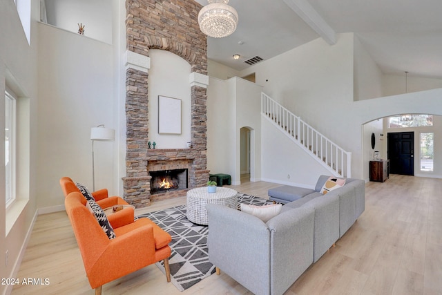 living room featuring high vaulted ceiling, light hardwood / wood-style flooring, a notable chandelier, and a stone fireplace