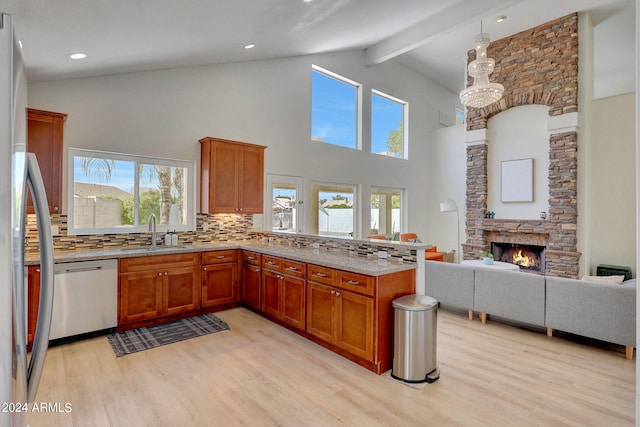 kitchen with a stone fireplace, tasteful backsplash, light hardwood / wood-style floors, stainless steel appliances, and sink