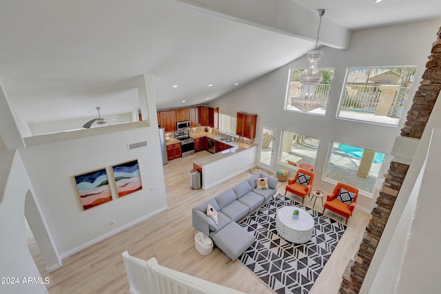 living room with ceiling fan with notable chandelier, beam ceiling, sink, high vaulted ceiling, and light wood-type flooring