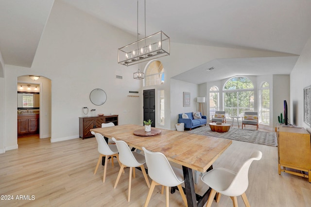 dining room with light wood-type flooring, an inviting chandelier, high vaulted ceiling, and sink