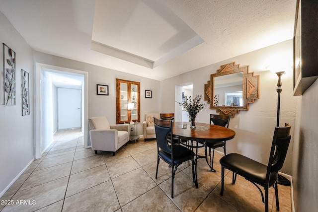 tiled dining room with a textured ceiling and a tray ceiling