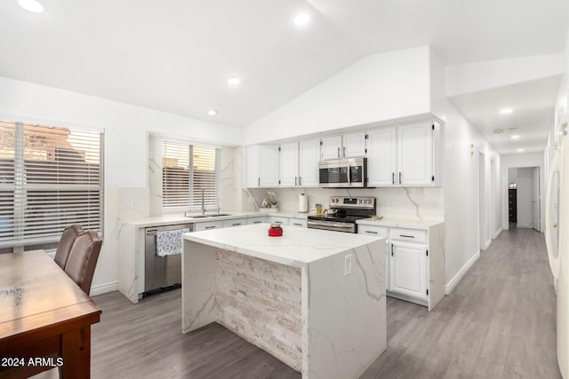 kitchen featuring appliances with stainless steel finishes, light wood-type flooring, white cabinets, a kitchen island, and lofted ceiling