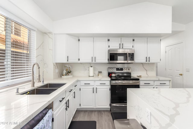 kitchen with white cabinets, appliances with stainless steel finishes, vaulted ceiling, and plenty of natural light