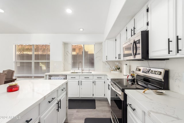 kitchen featuring appliances with stainless steel finishes, light stone counters, sink, hardwood / wood-style floors, and white cabinetry