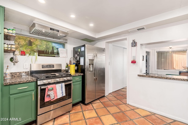 kitchen featuring wall chimney exhaust hood, dark stone countertops, appliances with stainless steel finishes, and green cabinetry