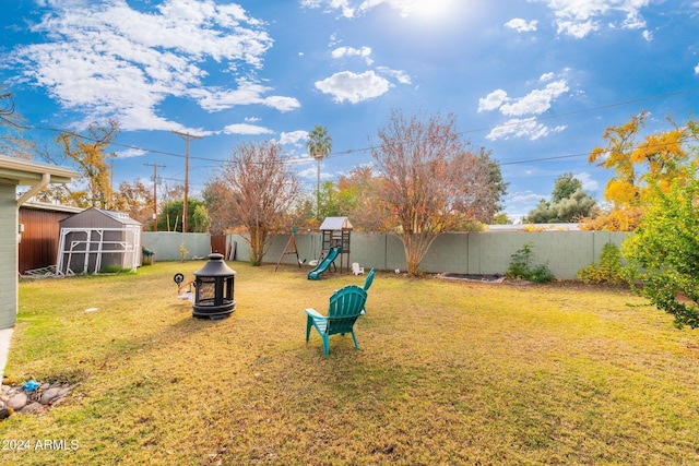 view of yard featuring a storage unit, a playground, and an outdoor fire pit