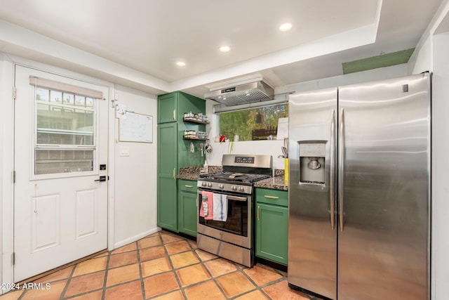 kitchen featuring wall chimney exhaust hood, green cabinets, dark stone countertops, and appliances with stainless steel finishes