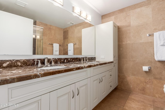 full bathroom with tile walls, visible vents, a sink, and tiled shower