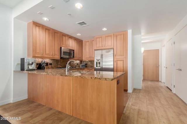 kitchen with stone countertops, visible vents, appliances with stainless steel finishes, a peninsula, and a sink