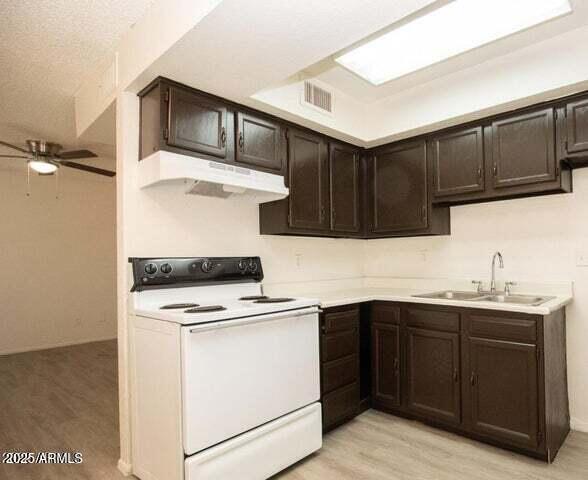 kitchen with white electric stove, under cabinet range hood, a sink, visible vents, and dark brown cabinets