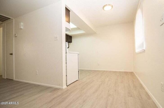 spare room with washer / dryer, light wood-type flooring, and baseboards