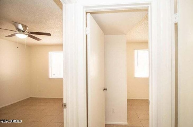 hallway with light tile patterned floors, baseboards, and a textured ceiling