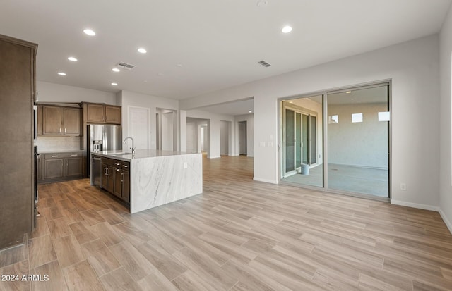 kitchen with a kitchen island with sink, sink, light wood-type flooring, tasteful backsplash, and light stone counters