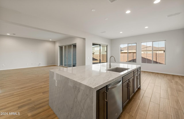 kitchen featuring dishwasher, a kitchen island with sink, sink, dark brown cabinets, and light stone counters