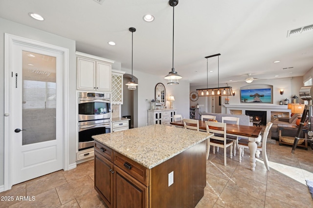 kitchen featuring visible vents, a center island, double oven, a lit fireplace, and recessed lighting