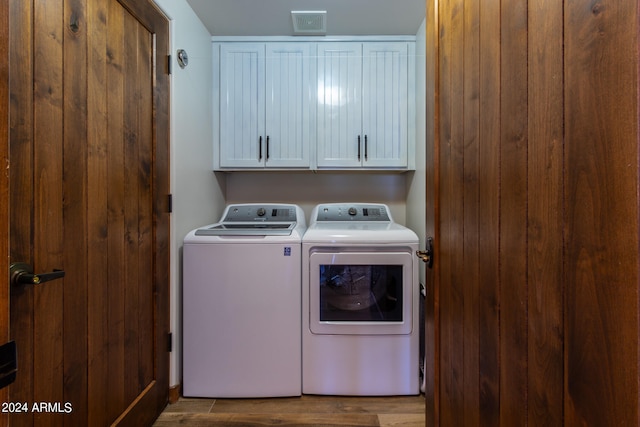 clothes washing area featuring cabinets, washing machine and clothes dryer, and dark hardwood / wood-style floors