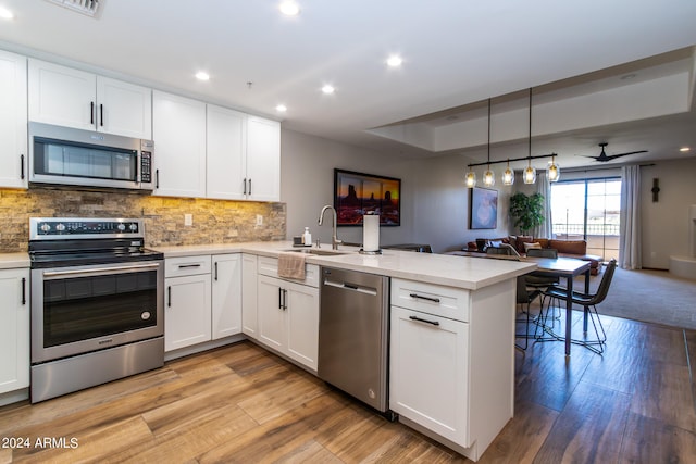 kitchen featuring kitchen peninsula, appliances with stainless steel finishes, light hardwood / wood-style flooring, hanging light fixtures, and white cabinetry