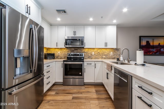 kitchen with light stone counters, stainless steel appliances, light wood-type flooring, and white cabinetry