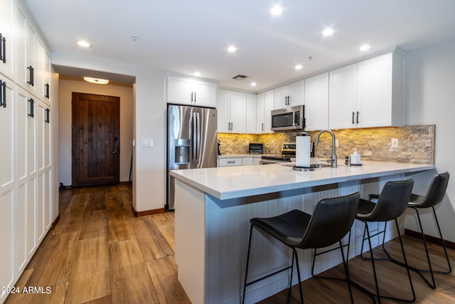 kitchen with white cabinets, a kitchen breakfast bar, stainless steel appliances, and light hardwood / wood-style floors