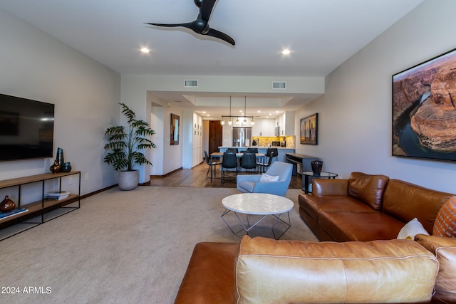 carpeted living room featuring ceiling fan with notable chandelier