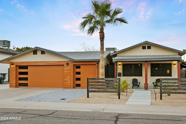view of front of property with a garage, decorative driveway, central AC, and stucco siding