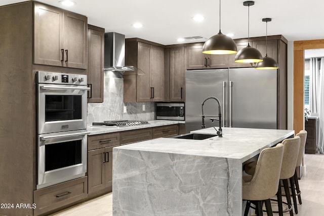 kitchen with visible vents, backsplash, stainless steel appliances, wall chimney exhaust hood, and a sink