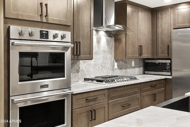 kitchen featuring decorative backsplash, wall chimney range hood, light stone counters, and stainless steel appliances