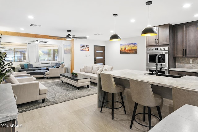 kitchen with visible vents, a sink, dark brown cabinets, double oven, and a kitchen breakfast bar