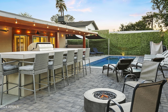 patio terrace at dusk with outdoor dry bar, a fenced in pool, an outdoor fire pit, central AC unit, and a grill