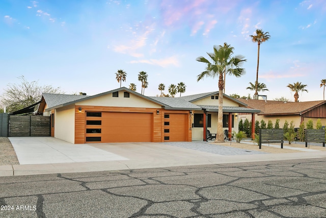 view of front facade featuring a shingled roof, fence, concrete driveway, a garage, and a gate