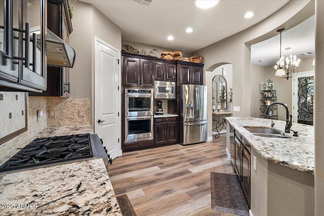 kitchen with arched walkways, stainless steel appliances, light wood-style flooring, a sink, and dark brown cabinetry