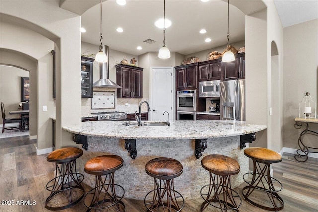 kitchen featuring visible vents, arched walkways, appliances with stainless steel finishes, wall chimney range hood, and a sink