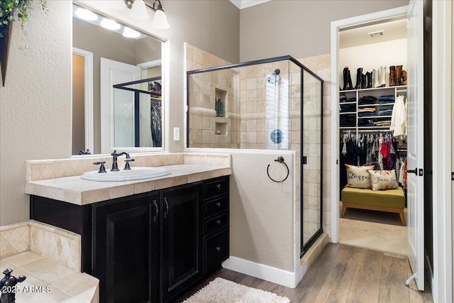 bathroom featuring a stall shower, a textured wall, wood finished floors, a walk in closet, and vanity