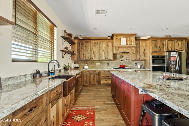 kitchen with light stone countertops, stainless steel appliances, decorative backsplash, custom exhaust hood, and light wood-type flooring