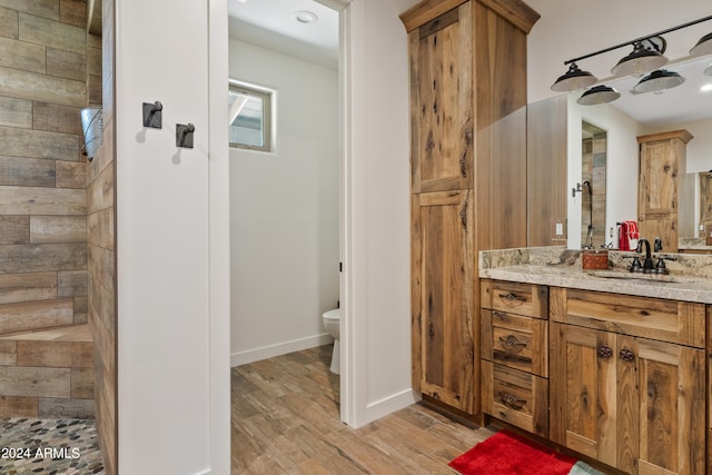 bathroom featuring tiled shower, wood-type flooring, toilet, and vanity