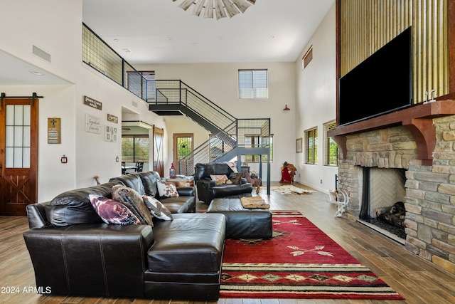 living room featuring a towering ceiling, wood-type flooring, and a stone fireplace