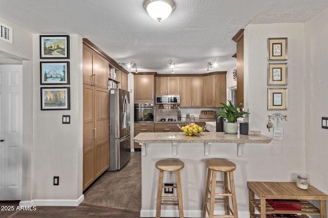 kitchen featuring a textured ceiling, light stone counters, a kitchen breakfast bar, kitchen peninsula, and appliances with stainless steel finishes