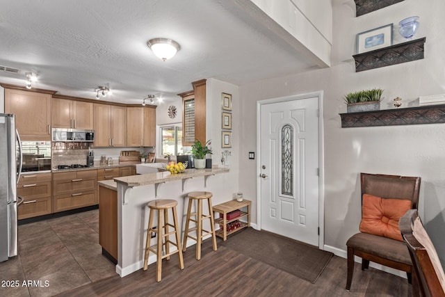 kitchen featuring kitchen peninsula, a breakfast bar, decorative backsplash, appliances with stainless steel finishes, and sink