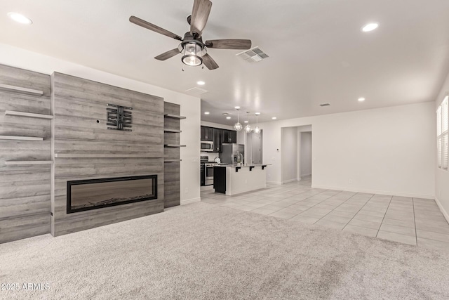 unfurnished living room with ceiling fan, light tile patterned floors, and a large fireplace