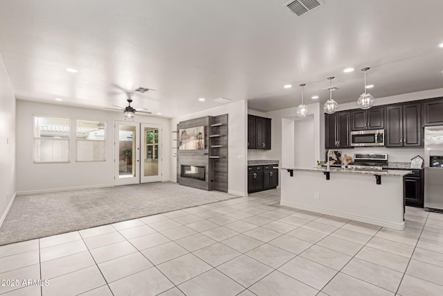 kitchen featuring ceiling fan, appliances with stainless steel finishes, an island with sink, a breakfast bar area, and light carpet