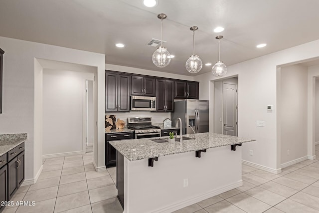 kitchen with a kitchen bar, stainless steel appliances, sink, a kitchen island with sink, and light stone counters